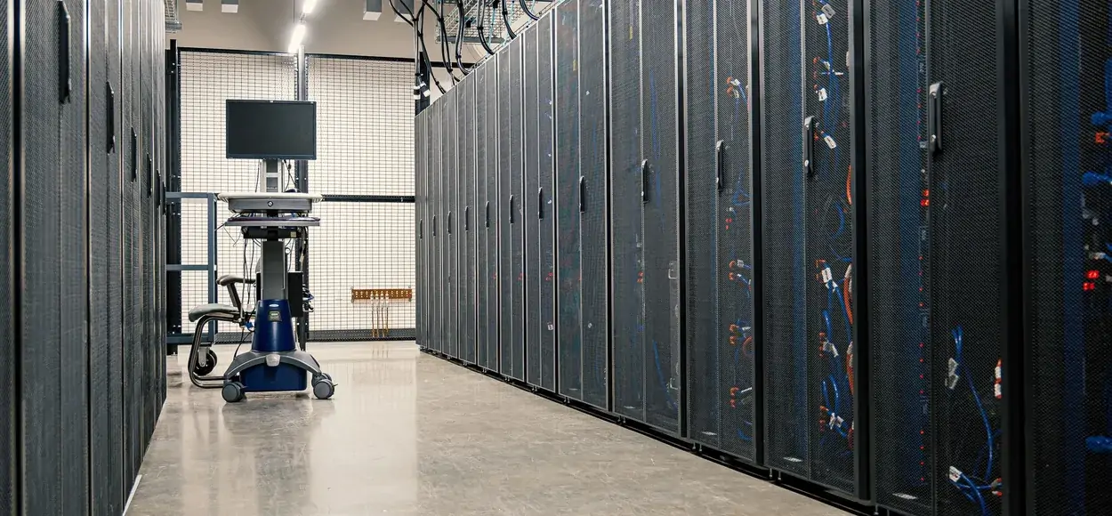 An aisle in a server room lined with closed racks, with a mobile workstation and its monitor at the far end